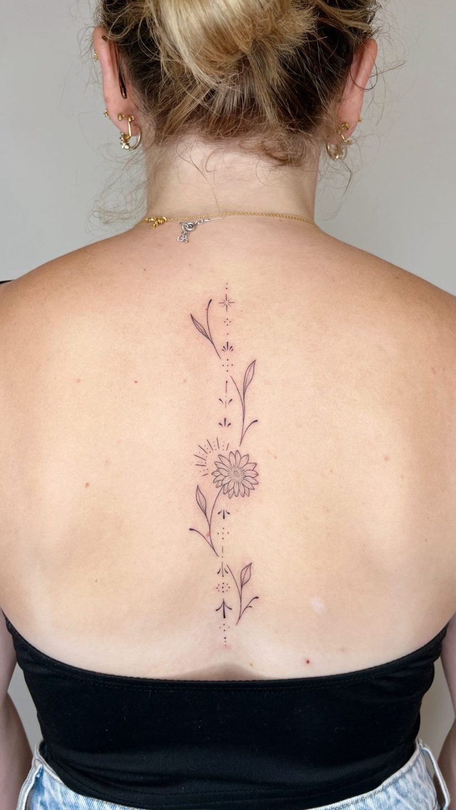 Tatouage fine line le long de la colonne : fleur, feuillages et ornements